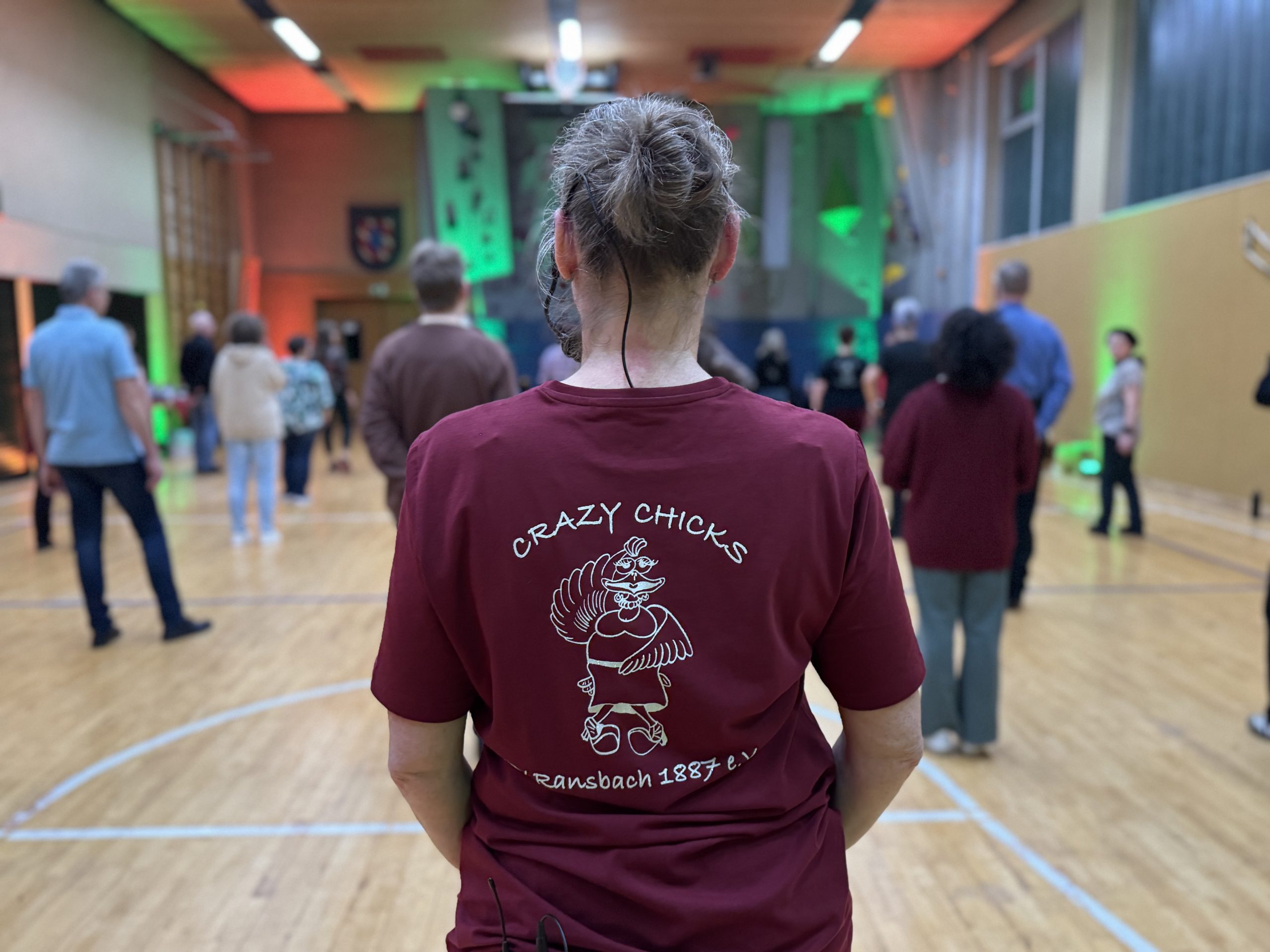 Die Trainerin der Linedancegruppe steht mit dem Rücken zur Kamera und man kann das Logo der Linedancegruppe "Crazy Chicken" sehen.